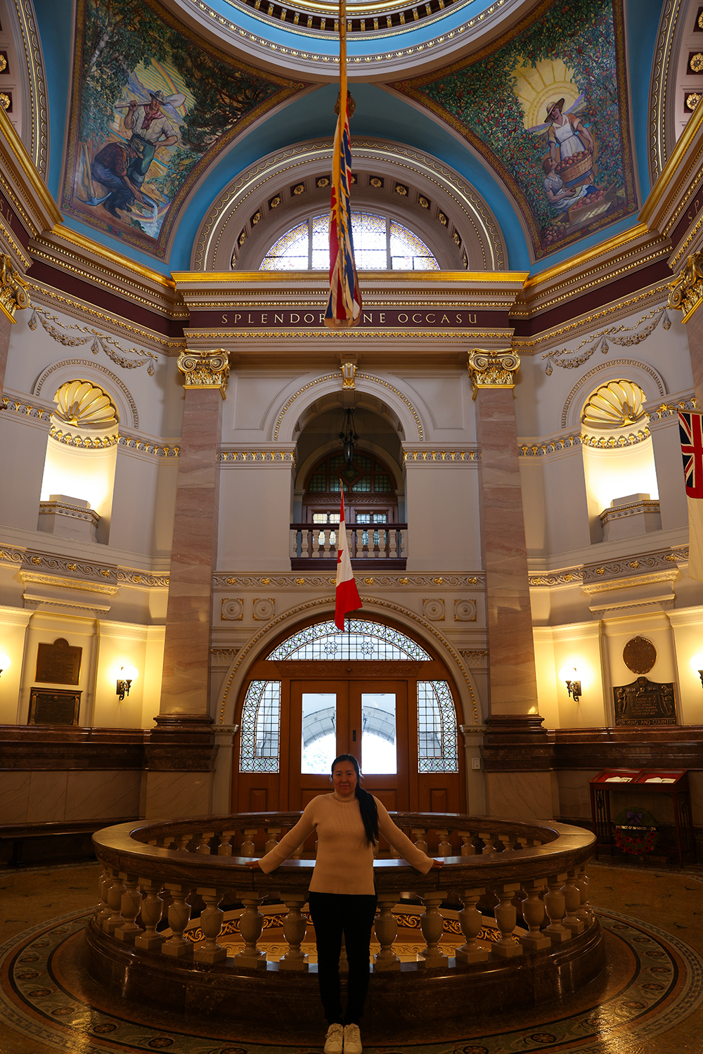 Asian woman wears a light pink sweater, black jeans, and white shoes inside the British Columbia Parliament buildings