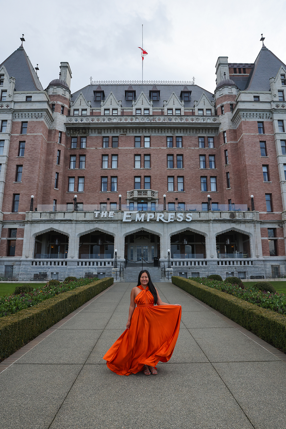 Asian woman wearing a orange flowy dress in the front of Fairmont Empress Hotel